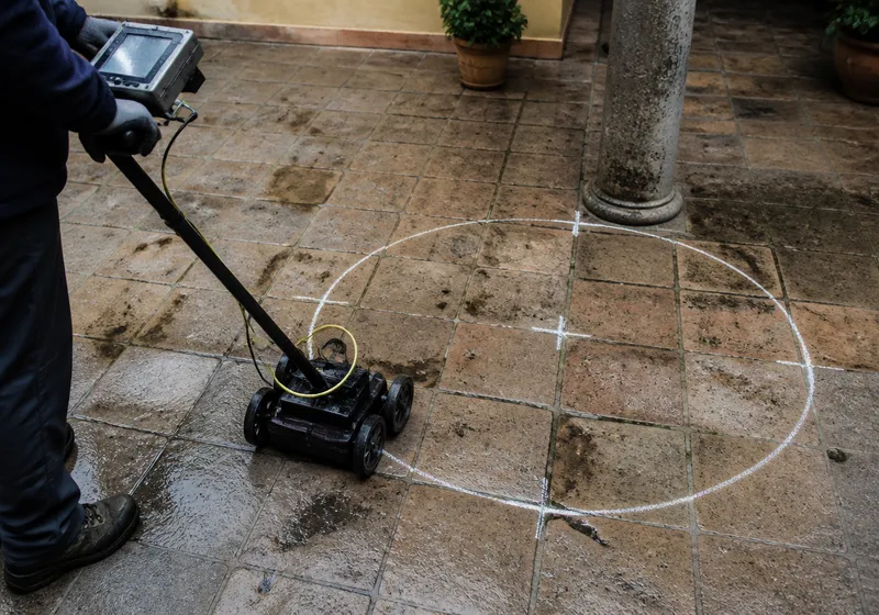 Técnico de espalda localizando una arqueta tapada en un patio de Sevilla con equipo de detección